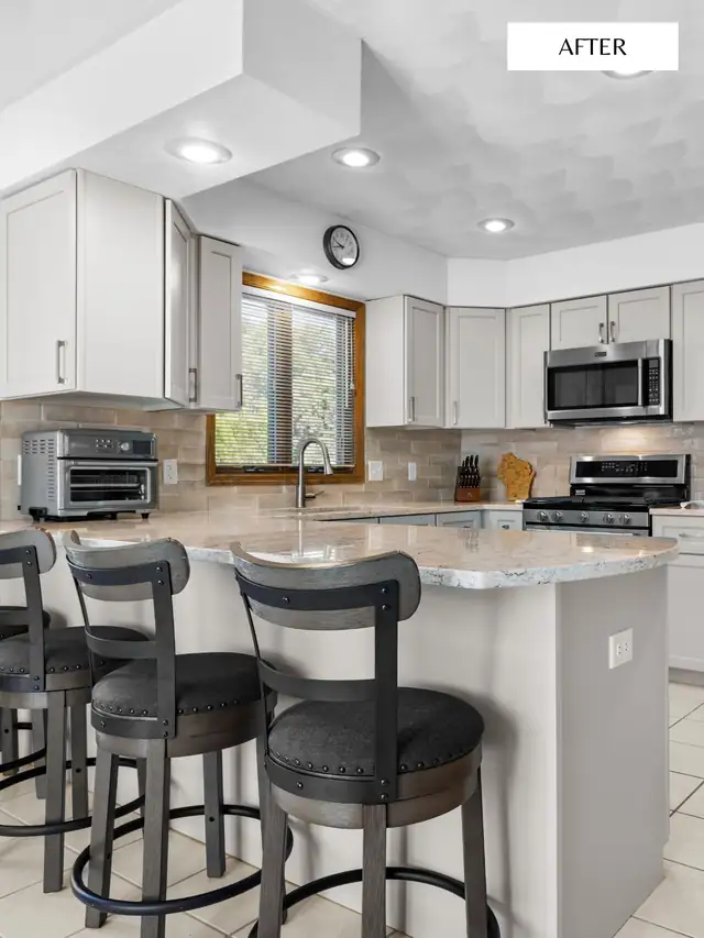 Kitchen with white shaker cabinets, a granite peninsula and three swivel bar stools