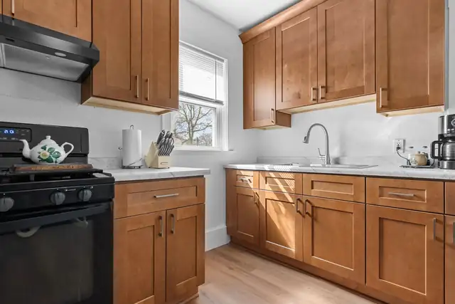Kitchen with warm maple shaker cabinets, white counters, a black range and morning light from two windows